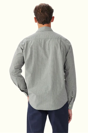 A man is seen from behind wearing the RM Williams Quinn Classic Poplin Shirt, a long-sleeve, yarn-dyed check shirt in black and white, paired with navy pants. His right hand rests on his hip against a plain off-white background.