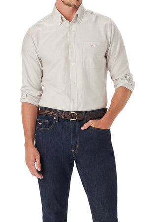 A man wears the RM Williams Regular Oxford Stripe Shirt—light-colored with thin vertical stripes in soft cotton—paired with dark blue jeans and a brown braided belt. His left hand is in his pocket, and his head is not visible.