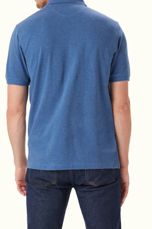 A man is shown from the back, wearing the RM Williams Rod Polo—short-sleeved, blue, organic cotton with subtle Longhorn embroidery—and dark jeans against a plain light background.