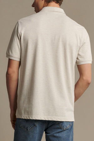 A person wearing the RM Williams Rod Polo, a short-sleeved light beige shirt made from Australian cotton, along with blue jeans is shown from the back against a plain background.