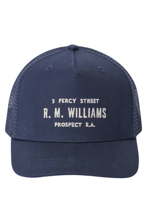 The RM Williams Stencil Trucker Cap is a navy blue cap with white mesh sides, featuring an embroidered stencil graphic and "5 Percy Street R. M. Williams Prospect S.A." text on the front, plus a snap adjuster for comfort.