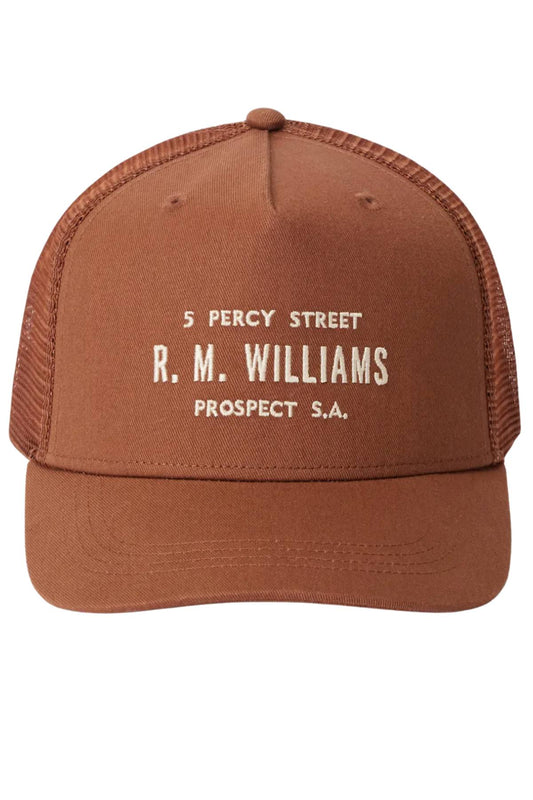 The RM Williams Stencil Trucker Cap features brown mesh, organic cotton twill, a white "5 PERCY STREET R. M. WILLIAMS PROSPECT S.A." stencil graphic on the front, and a classic snapback adjuster for a perfect fit.
