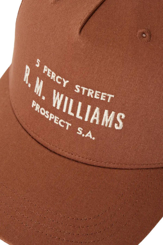 Close-up of the RM Williams Stencil Trucker Cap, made from organic cotton twill in brown, with white "5 Percy Street R. M. Williams Prospect S.A." embroidery and a snap adjuster at the back for a customized fit.