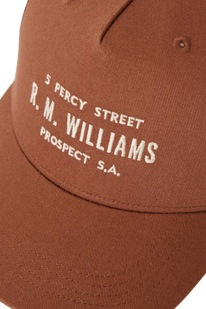 Close-up of the RM Williams Stencil Trucker Cap, made from organic cotton twill in brown, with white "5 Percy Street R. M. Williams Prospect S.A." embroidery and a snap adjuster at the back for a customized fit.