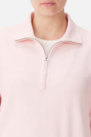 A person wears the RM Williams Trickett Zip Neck Sweatshirt in light pink organic cotton over a white undershirt. Only their lower face and upper torso are visible against a plain background.