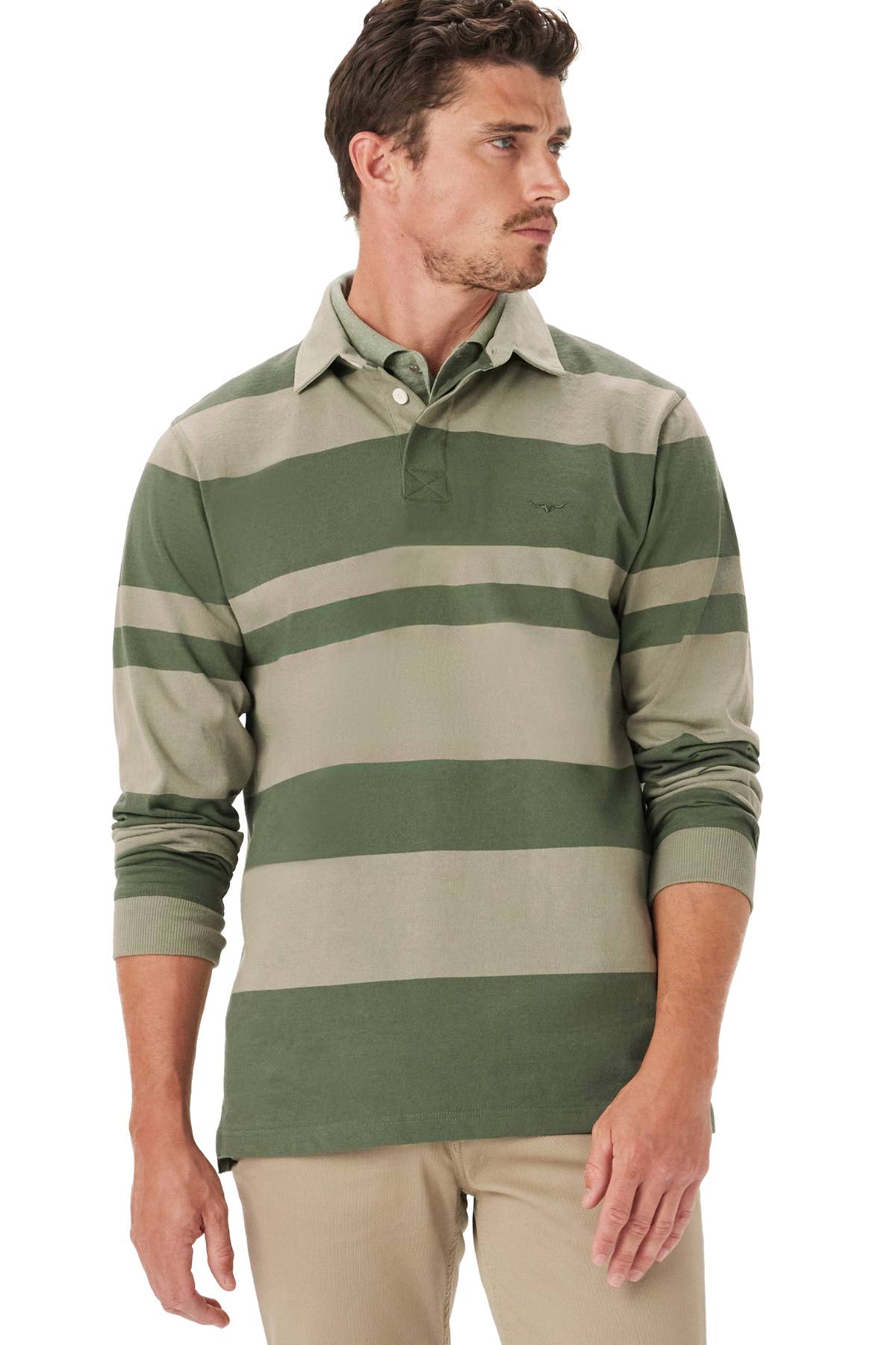 A man wears the RM Williams Tweedale Rugby, a green and beige striped 100% cotton jersey, paired with beige pants, standing slightly to the side and looking off to his left.