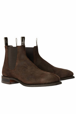 The RM Williams Comfort Craftsman Boot is a pair of brown waxed suede Chelsea boots with black elastic panels, pull tabs, low wooden heels, and a comfort insole, shown on a white background.