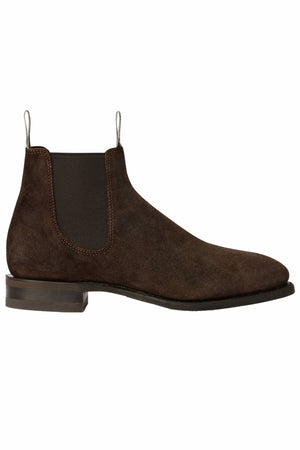 The RM Williams Comfort Craftsman Boot is a dark brown waxed suede Chelsea boot with elastic side panels, white pull tabs, and a low stacked heel, shown in side profile against a white background.