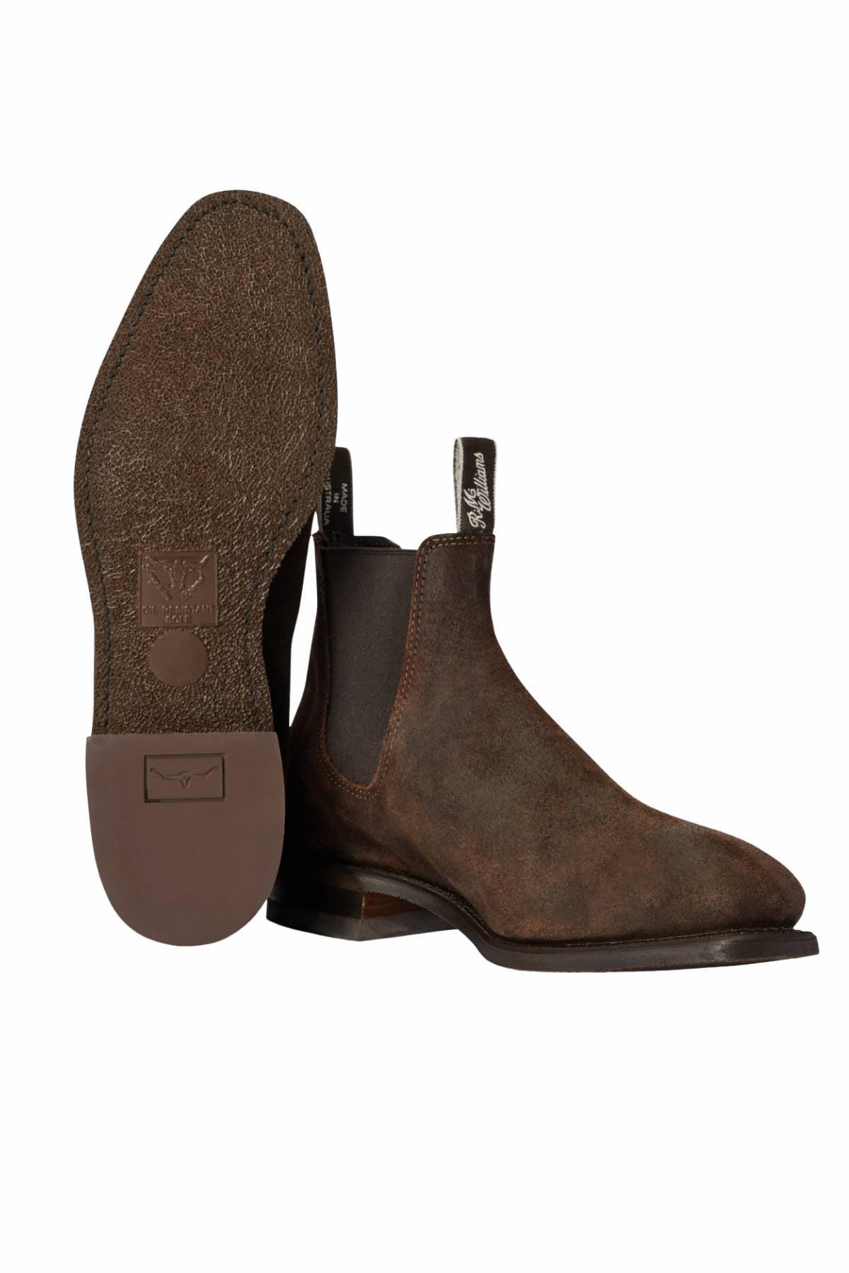 The RM Williams Comfort Craftsman Boot, in brown leather, features Goodyear welt construction, black elastic side panels, and front and back pull tabs. One boot stands upright while the other displays its textured sole and heel.