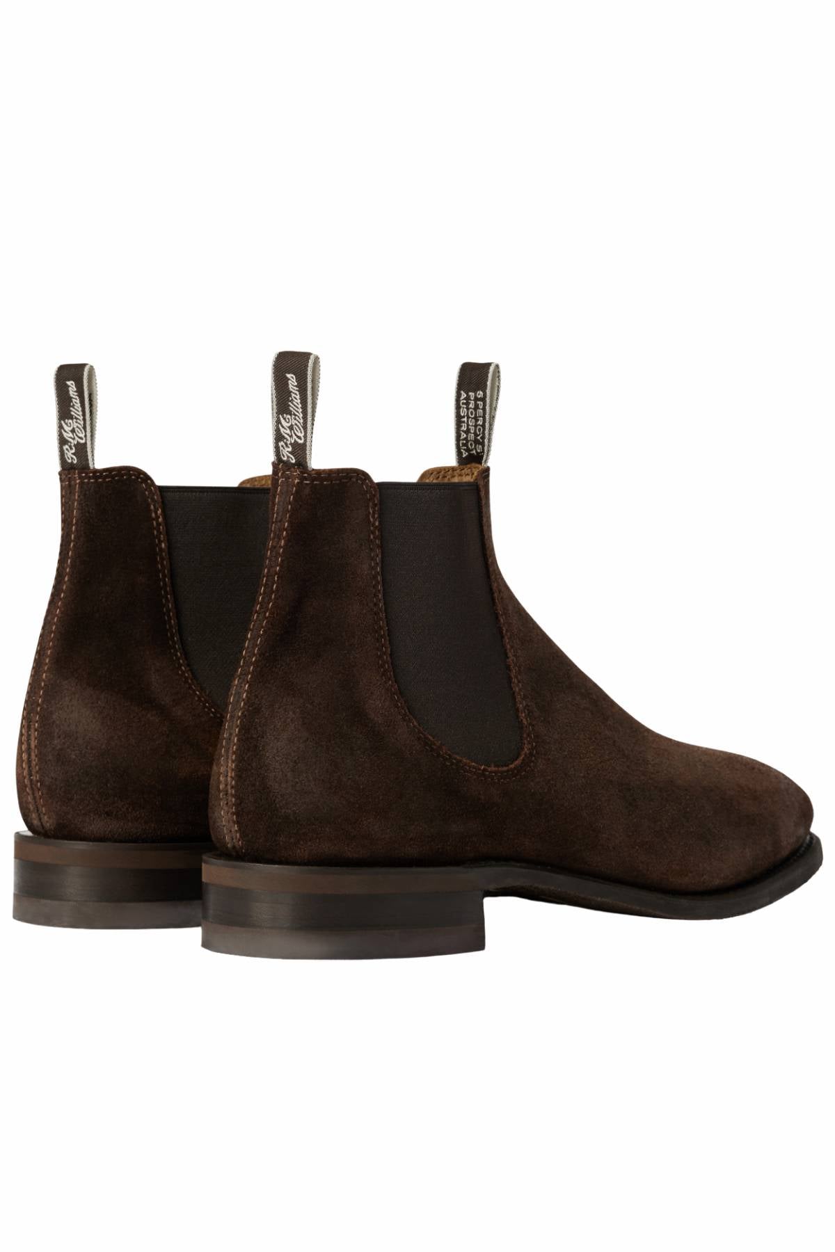 The RM Williams Comfort Craftsman Boot is a dark brown waxed suede Chelsea boot with elastic side panels, white-branded pull tabs, a comfort insole, and stacked wooden heels, shown from the back and side on a white background.