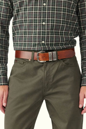 A person wearing a dark plaid button-down shirt tucked into olive green pants, styled with an RM Williams Drover Belt with a silver buckle. The image is cropped from mid-torso to upper thighs.