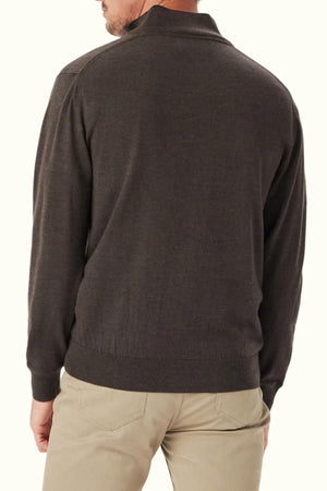 A man wearing an RM Williams Ernest 1/4 Zip Merino Knit sweater in dark brown and beige pants stands with his back to the camera against a plain light background.