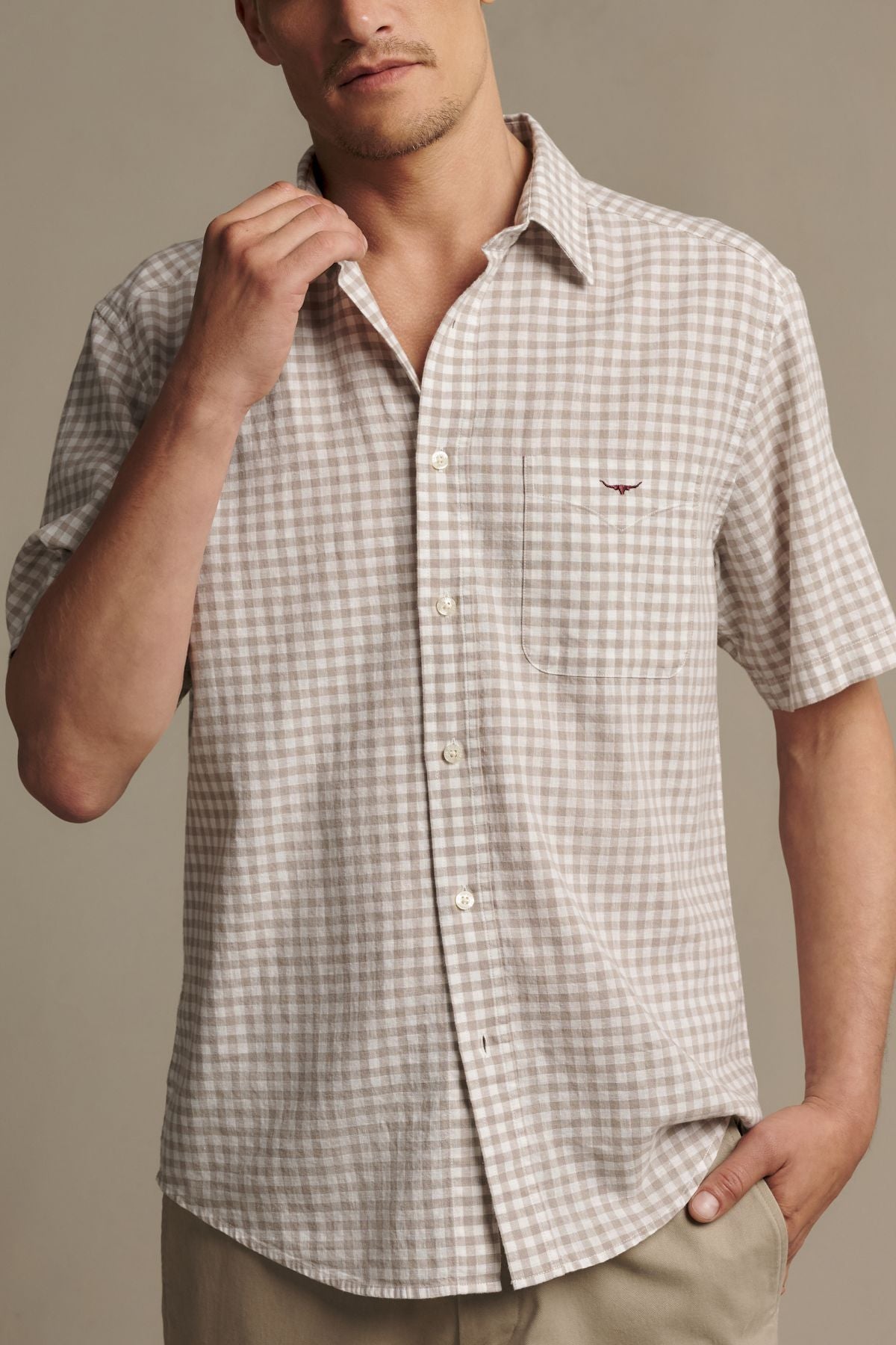 A man wearing the RM Williams Johnson Check Short Sleeve Shirt—a beige and white checkered short-sleeve button-up with a pocket—stands against a plain background.
