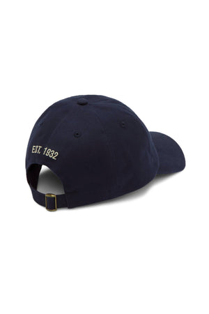 The RM Williams Mini Longhorn Twill Cap is shown from the back in navy organic cotton, with "EST. 1932" embroidered in white above an adjustable strap and brass buckle.