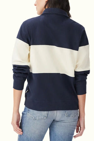 A person shown from the back wearing the RM Williams Trickett Panel Sweatshirt in navy and white stripes, paired with light blue jeans. The sweatshirt features a bold horizontal white panel across the middle.