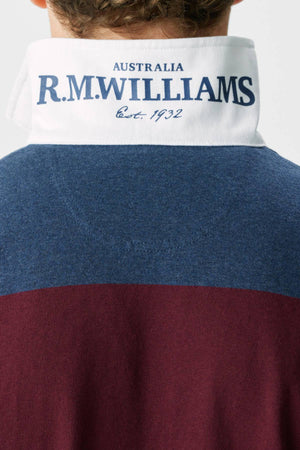 The back view of a person wearing the RM Williams Tweedale Rugby, an organic cotton polo with a white collar featuring blue "AUSTRALIA R.M. WILLIAMS Est. 1932" text and blue and maroon sections.