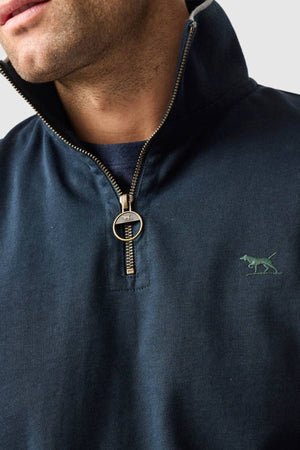 A close-up shows a person wearing a navy Rodd & Gunn Gunn 14oz 1/4 Zip Sweat with a circular zipper pull and a small green embroidered dog logo on the left chest, revealing their lower face and neck.
