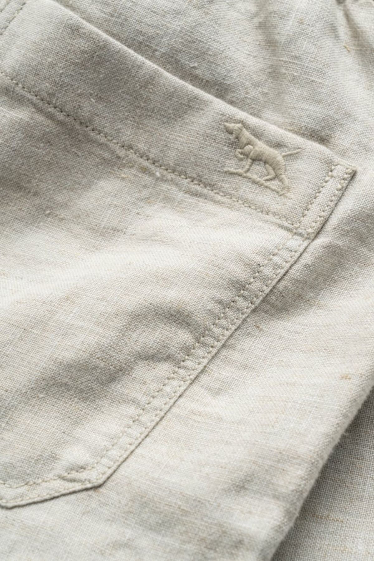 Close-up of the Rodd & Gunn Linen Resort Short in light beige, showing detailed pocket stitching and a small embroidered dog logo near the seam.