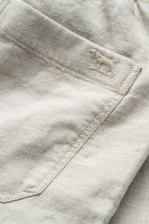 Close-up of the Rodd & Gunn Linen Resort Short in light beige, showing detailed pocket stitching and a small embroidered dog logo near the seam.