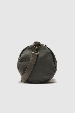 The Rodd & Gunn Ponsonby Road Duffle Bag, in round olive green cotton canvas with a shoulder strap and brass hardware, stands upright against a plain light gray background.
