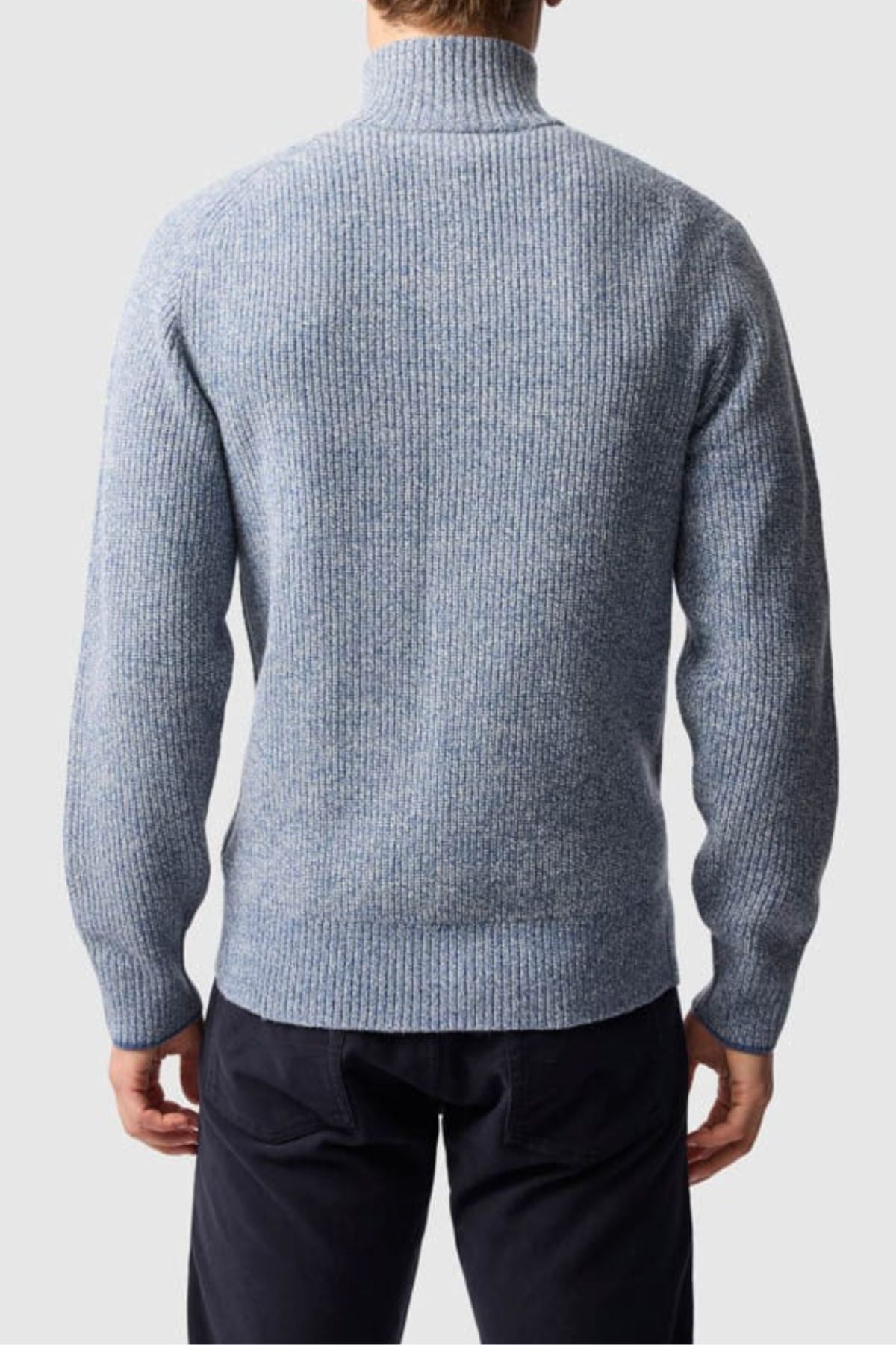 A man, seen from behind, wears a light blue Rodd & Gunn Robbies Road Knit sweater in fisherman’s rib and dark pants, set against a plain light gray background.