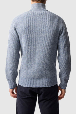 A man, seen from behind, wears a light blue Rodd & Gunn Robbies Road Knit sweater in fisherman’s rib and dark pants, set against a plain light gray background.