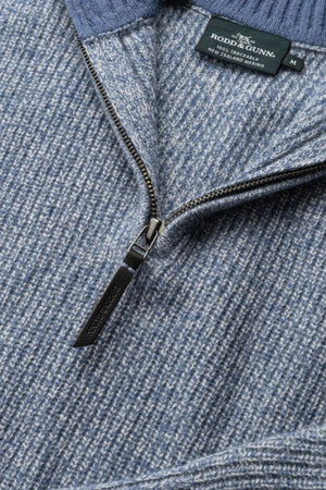 Close-up of the Rodd & Gunn Robbies Road Knit sweater in blue and grey, featuring a quarter-zip with dark metal pull tab and visible brand label inside the collar. Made from soft Merino wool in Fisherman's Rib Knit.