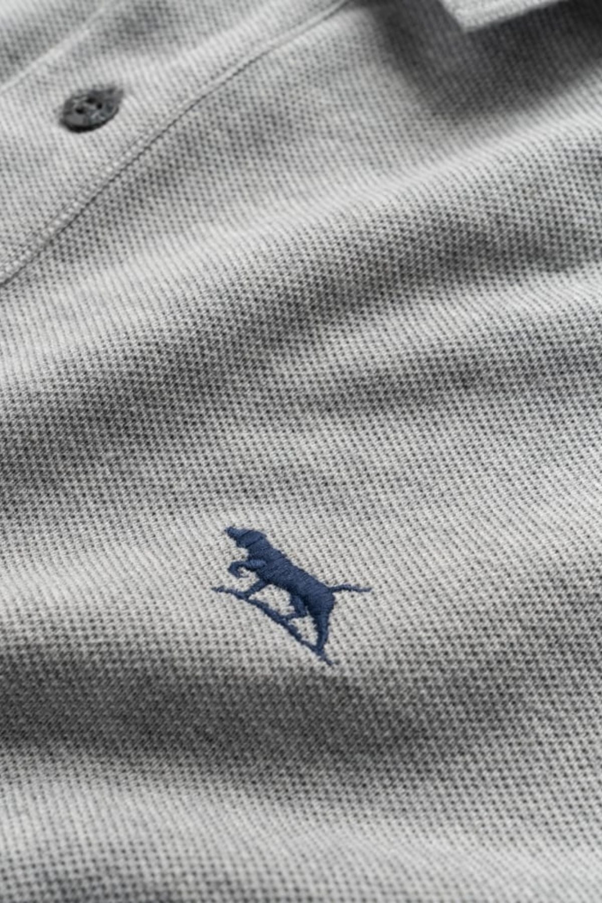 A close-up of the Rodd & Gunn The Gunn Polo in light gray, made from premium Australian cotton, with a dark blue stitched dog logo on the left chest and a collar button.