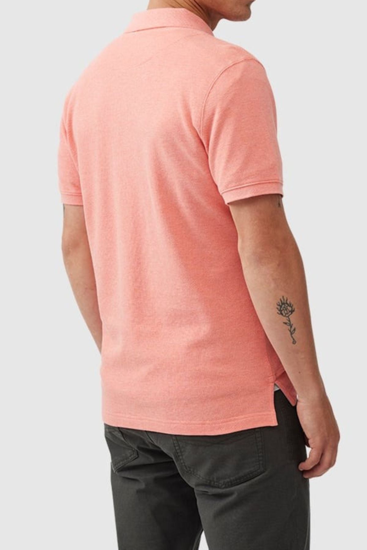 A person seen from the back wears a light pink Rodd & Gunn The Gunn Polo, modern fit and made from Australian cotton, paired with dark pants. A small black flower tattoo is visible on their right forearm.