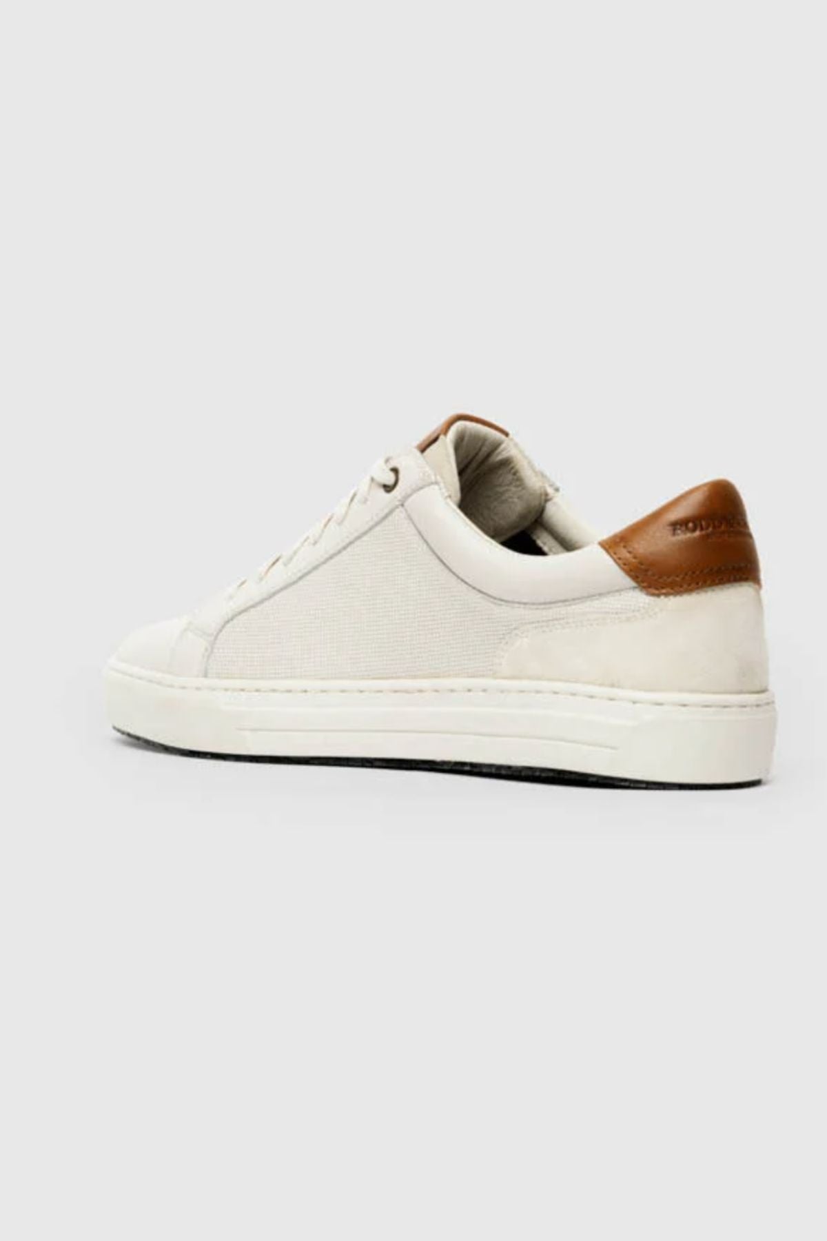 The Rodd & Gunn Transit Sneaker is a white low-top with premium leather, a brown heel accent, white laces, textured rubber sole, and removable foot bed for comfort—all presented on a light gray background.