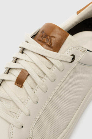 Close-up of the Rodd & Gunn Transit Sneaker, showcasing a cream design with textured side panels, white laces, and premium brown leather accents, including a tongue patch embossed with the signature kangaroo logo.