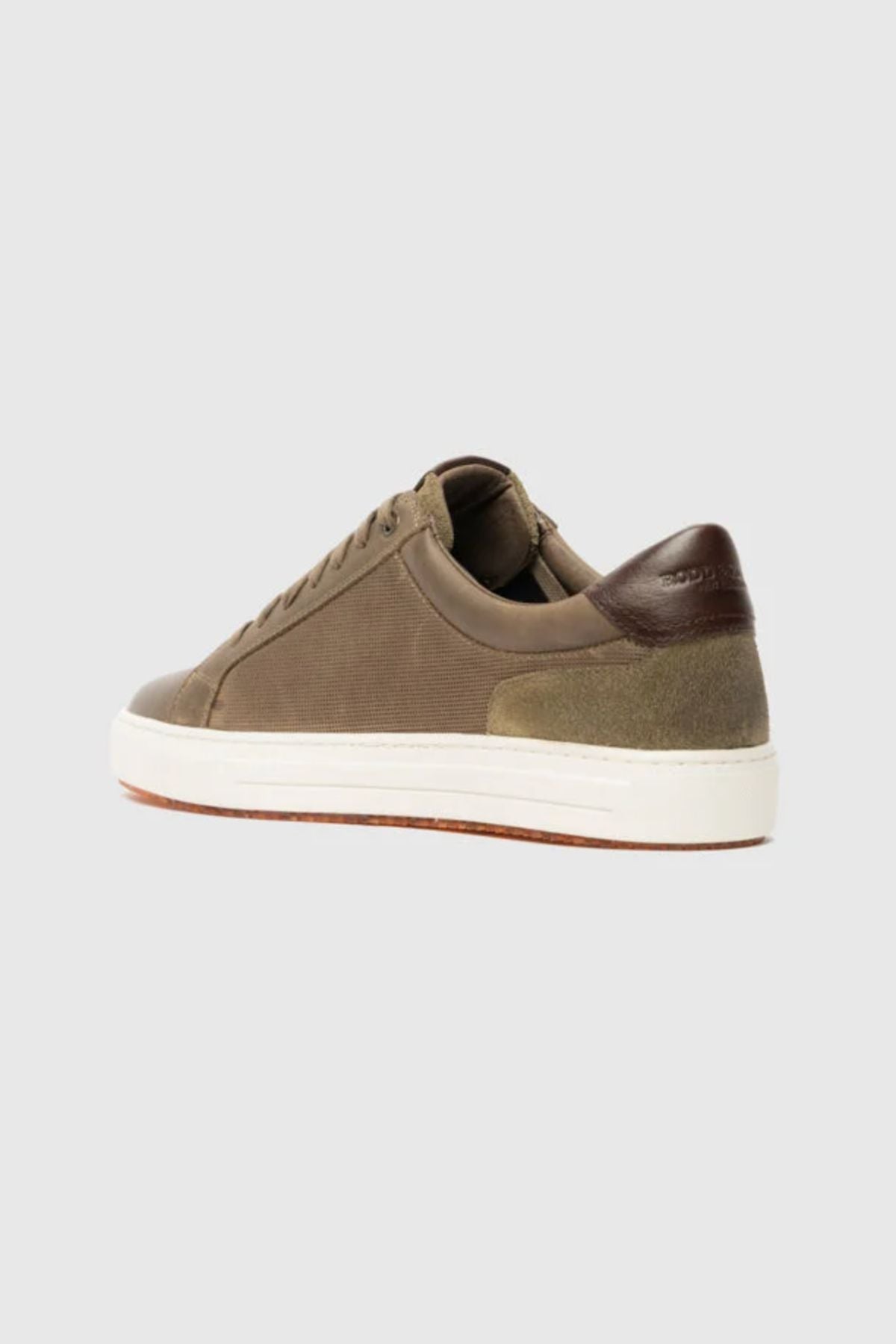The Rodd & Gunn Transit Sneaker features an olive green upper, white sole, brown leather heel accent, suede details, and a translucent outsole. Shown from a rear-side angle on a plain light grey background.