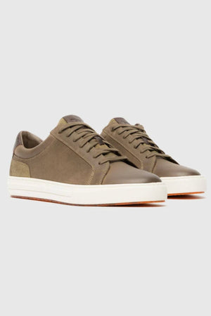 The Rodd & Gunn Transit Sneaker is a low-top pair in olive green with matching laces, white rubber soles, and brown outsoles, shown on a light gray background.