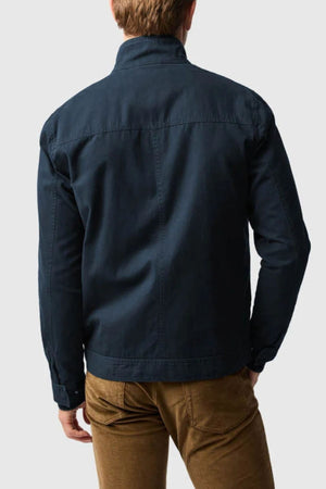 A person stands facing away, dressed in a dark blue Rodd & Gunn Armitage Jacket and light brown pants, set against a plain light gray backdrop.