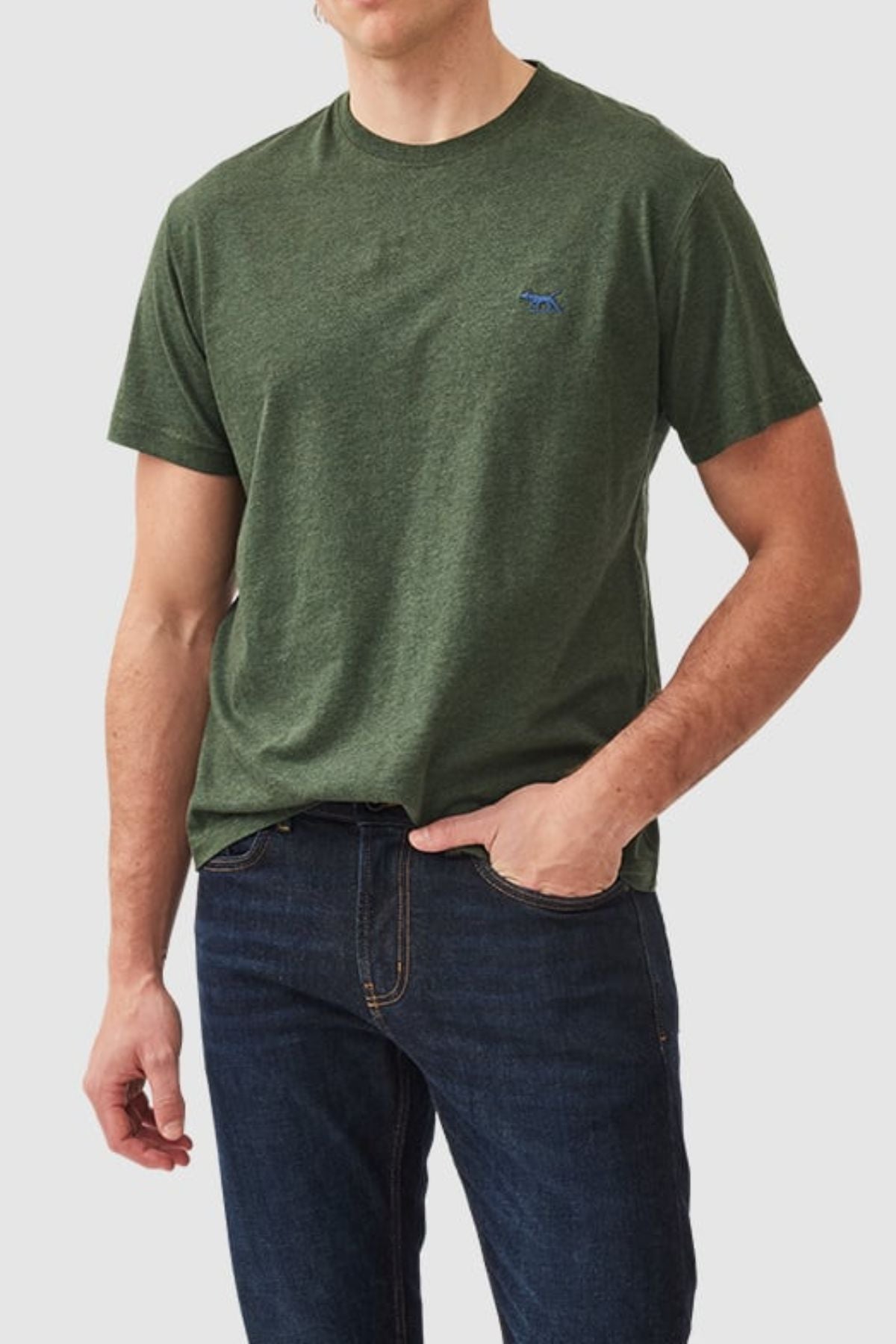 Wearing a dark green Australian Cotton Rodd & Gunn The Gunn T-Shirt with a blue chest logo and dark blue jeans, someone stands with one hand in their pocket against a plain gray background.