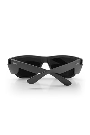 The SafeStyle Fusions XL Matte Black Frame Polarised Lens sunglasses are shown from the rear with their arms crossed over each other. The dark, polarized lenses are encased in a thick, durable frame. Both arms feature small white logos near the hinges, and the background is plain white.