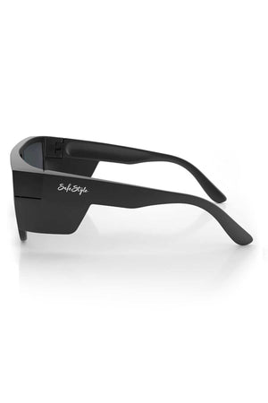 Introducing the SafeStyle Primes Matte Black Frame Reflectors Blue Lens: These black wraparound sunglasses boast thick, angular matte black frames and tinted blue lenses offering UV protection. Featuring a white "SafeStyle" logo on the side, these sunglasses are made from recyclable polycarbonate and are showcased against a white background.