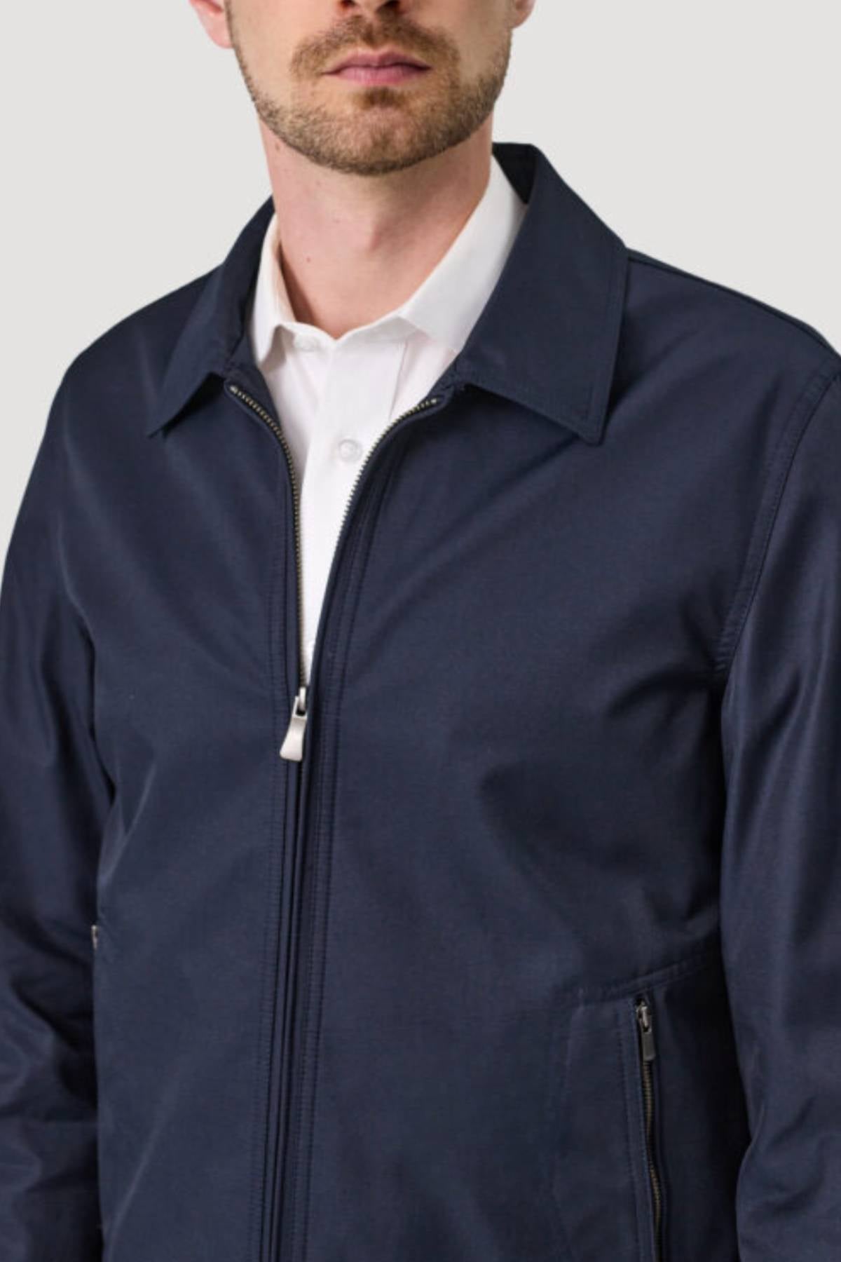 A man models the Savile Row James Zip Front Jacket in dark navy over a white collared shirt, shown from shoulders to waist against a plain light gray background.