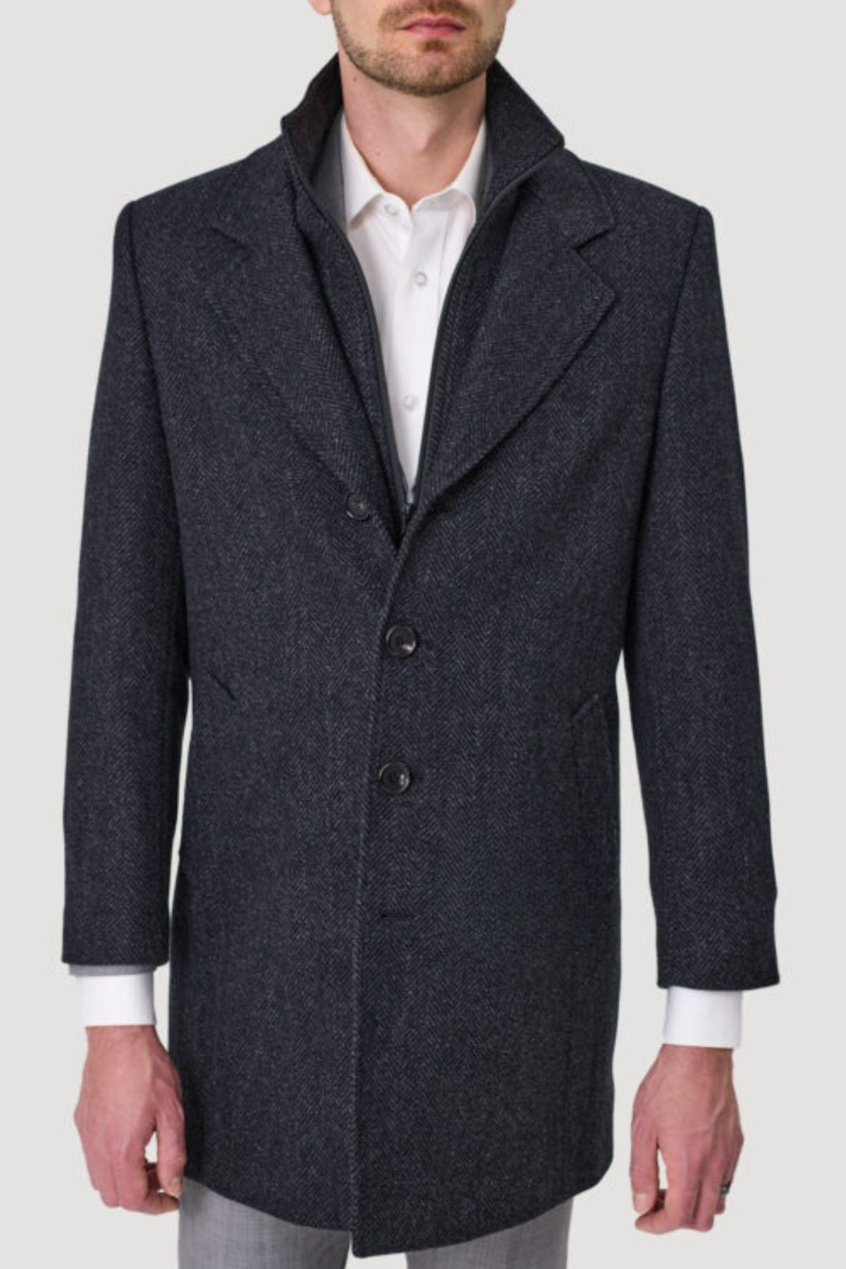 A man in a dark gray, textured Savile Row Jared Removable Collar Coat with three buttons over a white dress shirt and light gray pants stands against a plain light background, his face partially out of frame.