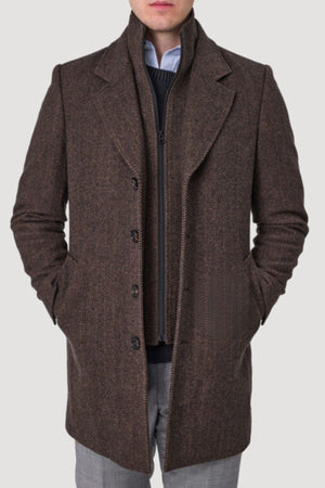 A man stands against a plain light background, hands in his pockets, wearing the Savile Row Jared Removable Collar Coat in brown over a dark zip-up sweater and light gray trousers.