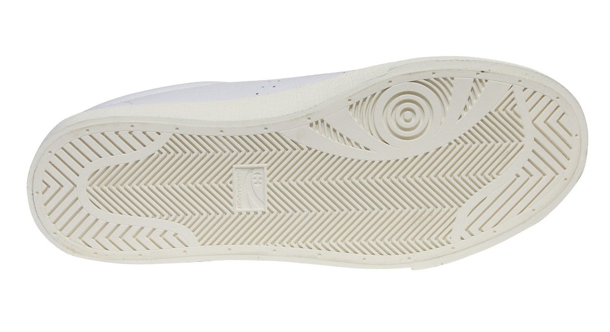 The image displays the sole of a white Superga 2843 Club S Comfort Leather Sneaker, featuring a vulcanised gum sole with a geometric pattern, herringbone grooves for traction, and a circular design at the heel.