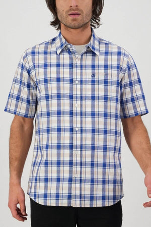 A person stands against a plain background wearing a blue and white checkered Swanndri Coleridge Short Sleeve Shirt, featuring a classic fit with short sleeves and a left-side pocket adorned with a small logo. The person's face is not visible.
