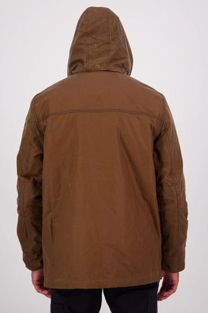 Someone is seen from the back, wearing the Swanndri Evans Flat v2 Oilskin Jacket—a brown waxed cotton hooded jacket—with arms relaxed at their sides, standing against a plain light background.