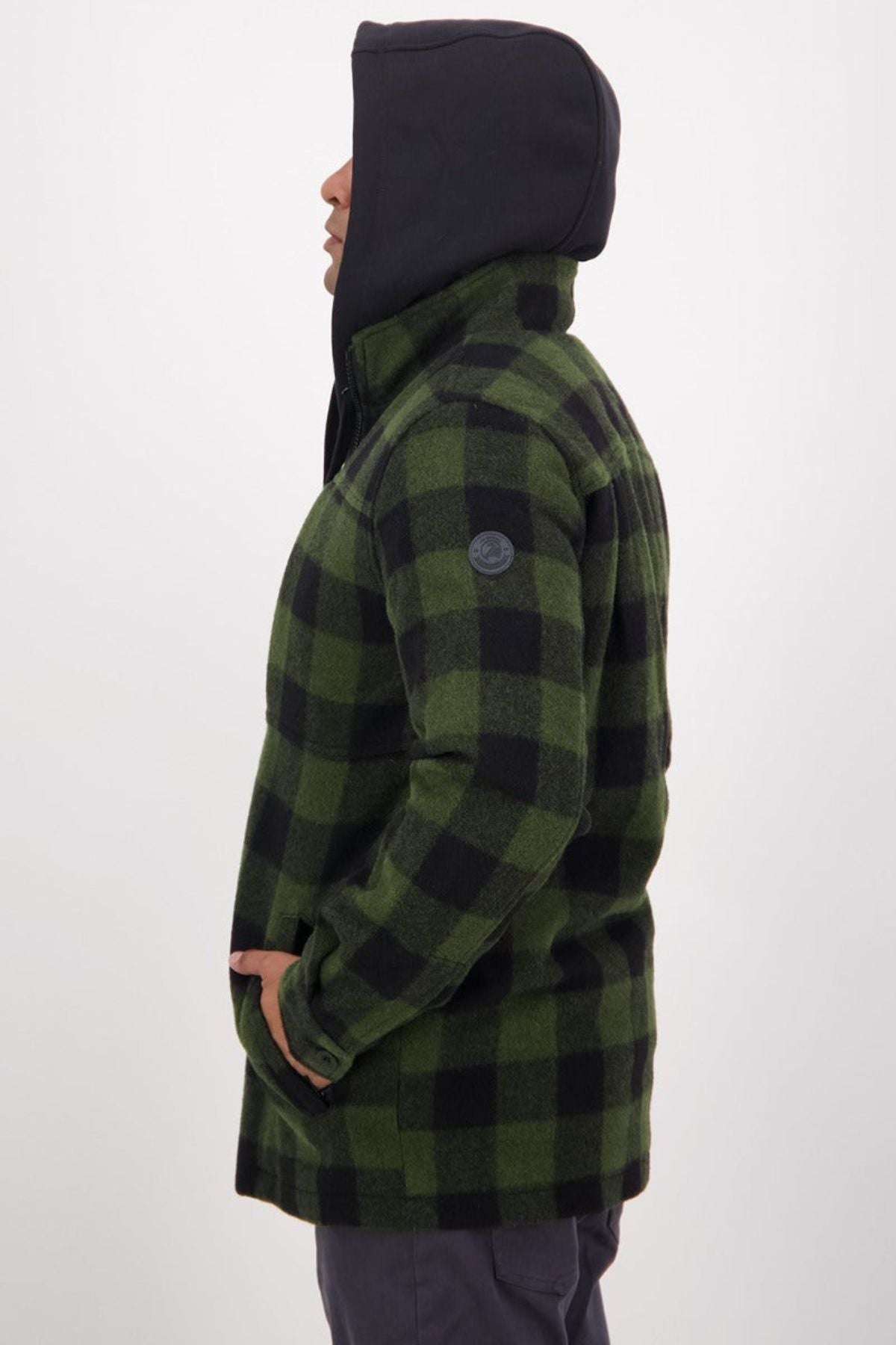 A person in profile view wears a green and black checkered Swanndri Hudson Jacket with a black hood, standing against a plain light background—ideal outdoor wear made from soft New Zealand wool.