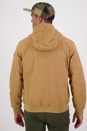 A person in a Swanndri Whitlow v2 Canvas Hoodie, olive green pants, and a green and tan plaid cap stands with their back to the camera against a plain light background.