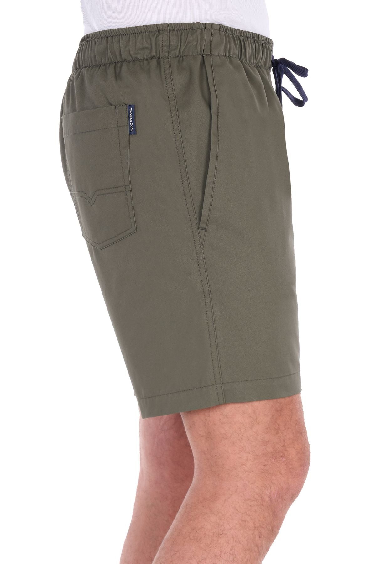 A person wearing the Thomas Cook Darcy Short in olive green, featuring an elasticated waist, side pockets, and a back pocket with a small tag, made from 100% cotton, is shown from the side against a white background.