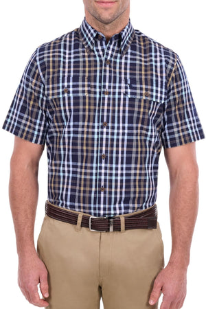 A man wears the Thomas Cook Finley Short Sleeve Shirt, a short-sleeve, button-down plaid shirt in blue, brown, and white. The classic workwear style is crafted from 100% cotton for comfort and breathability. He has it tucked into tan pants with a brown belt. His face is partially visible as he stands against a white background.