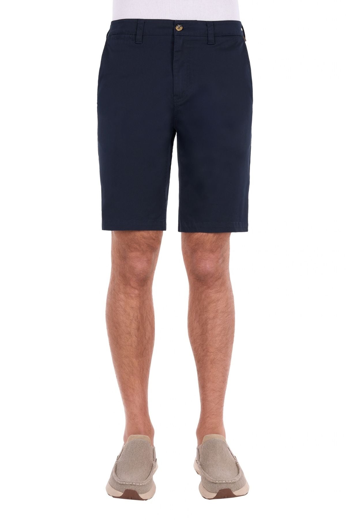 A man wearing the navy blue Thomas Cook Harrison Short, crafted from stretch fabric, paired with a white shirt and beige slip-on shoes, stands against a white background.