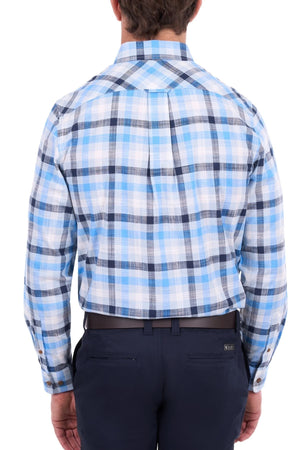 A man stands with his back to the camera, wearing a blue and white plaid long-sleeve Thomas Cook Jacob Shirt—an outback shirt crafted from 100% cotton—and dark navy pants.