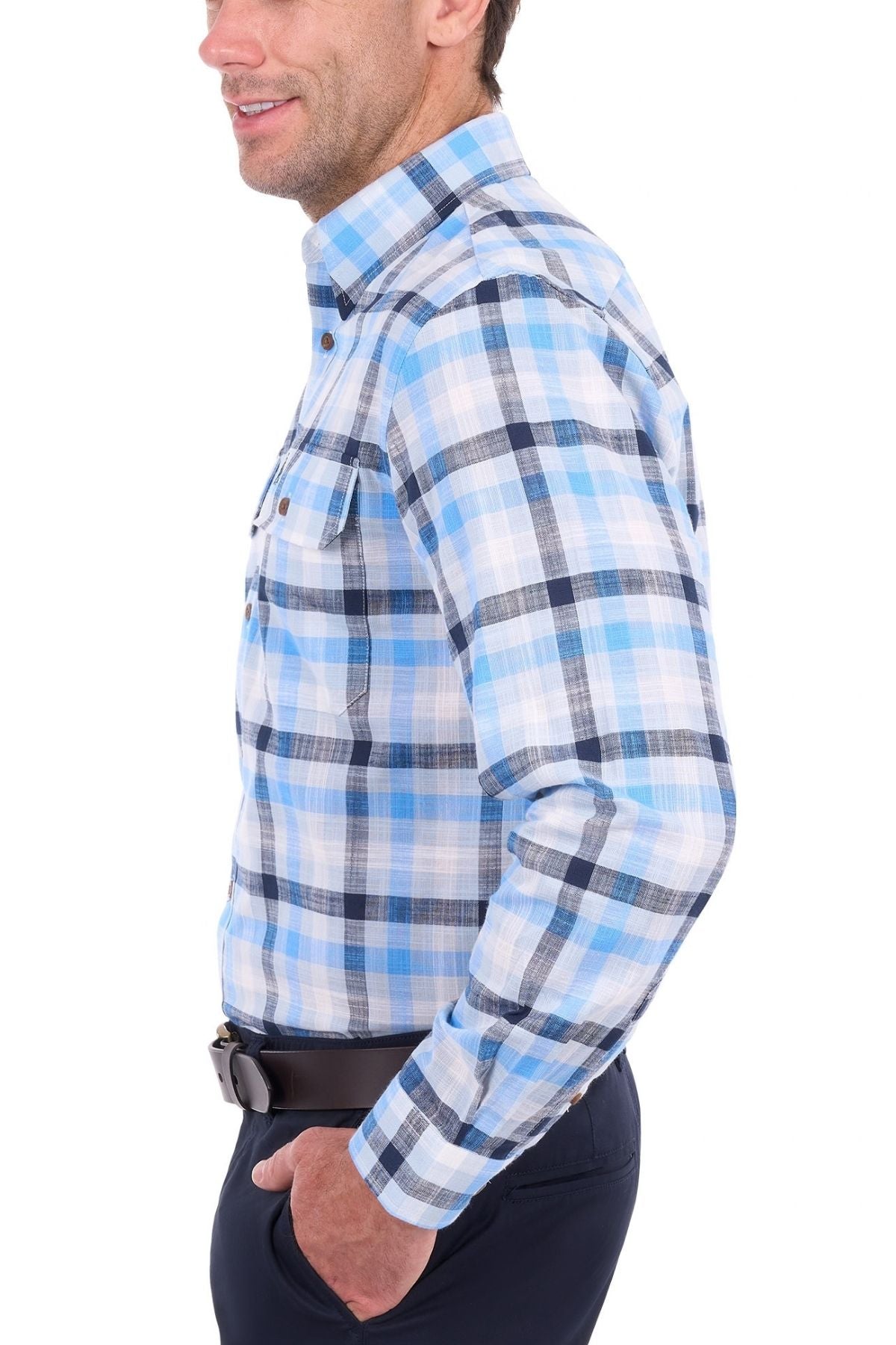A man wearing a blue and white plaid Thomas Cook Jacob Shirt, crafted from 100% cotton, stands sideways with his hands in his pockets, smiling against a white background.